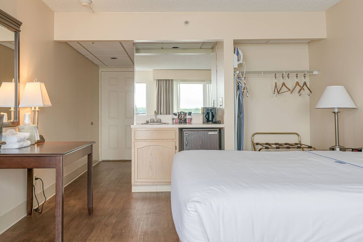 Hotelkamer met een bed, bureau met lamp, kitchenette en zichtbare badkamer door een open deur.