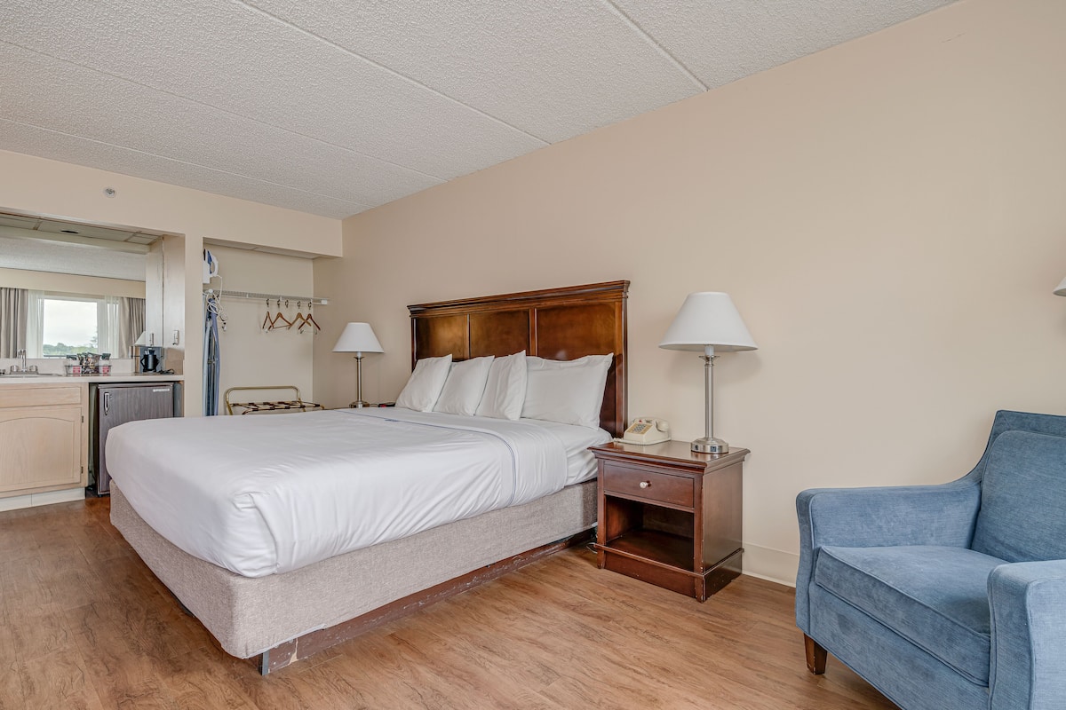 Een hotelkamer met een bed, nachtlampjes, een stoel en een klein bureau met een telefoon.