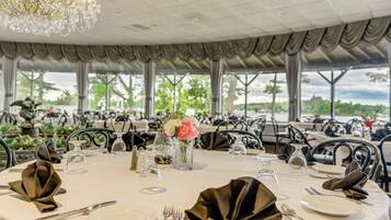 Une salle de banquet avec des tables rondes dressées pour le repas, agrémentée d’une décoration de table élégante et d’un lustre.