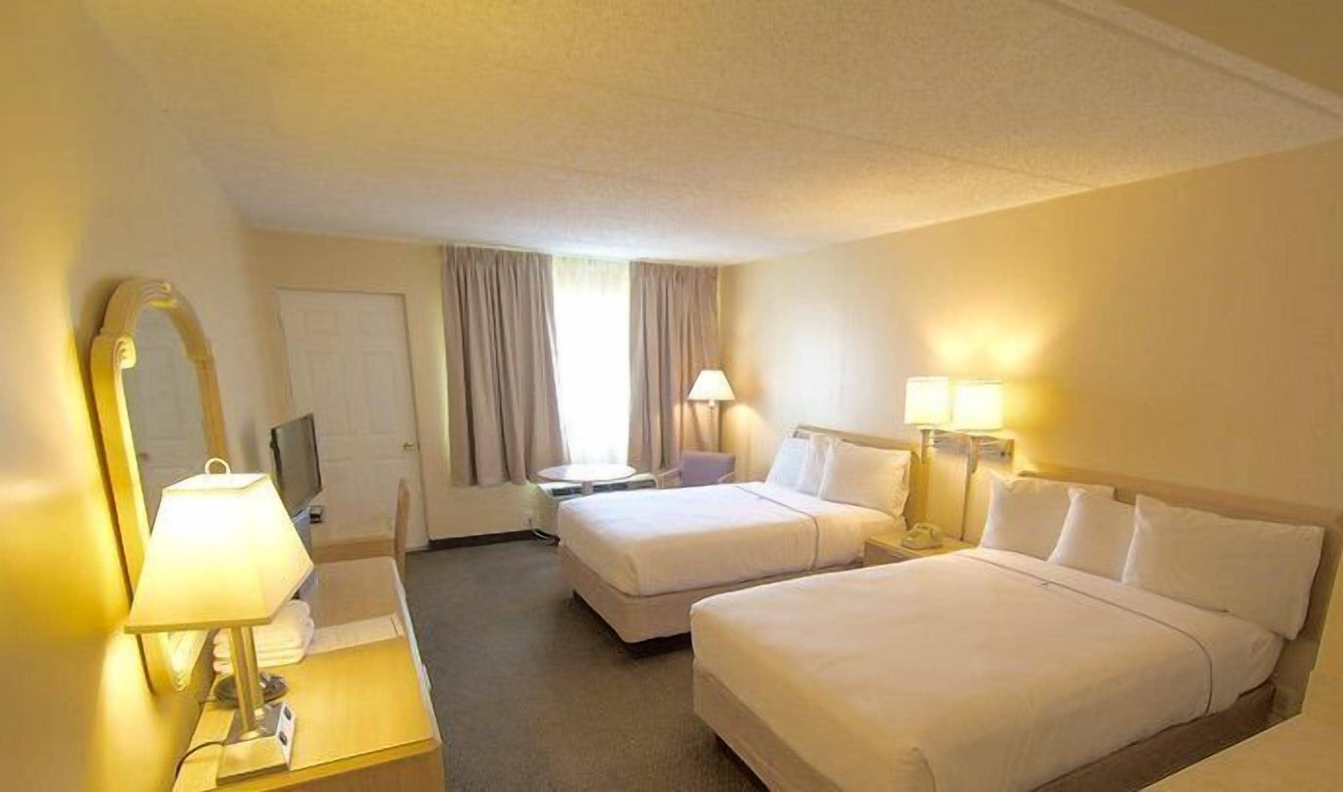A hotel room with two beds, a desk with a lamp, a chair, a TV, and a window with curtains.