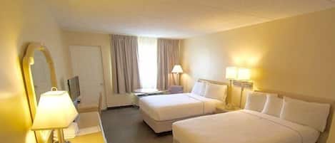 A hotel room with two beds, a desk with a lamp, a chair, a TV, and a window with curtains.