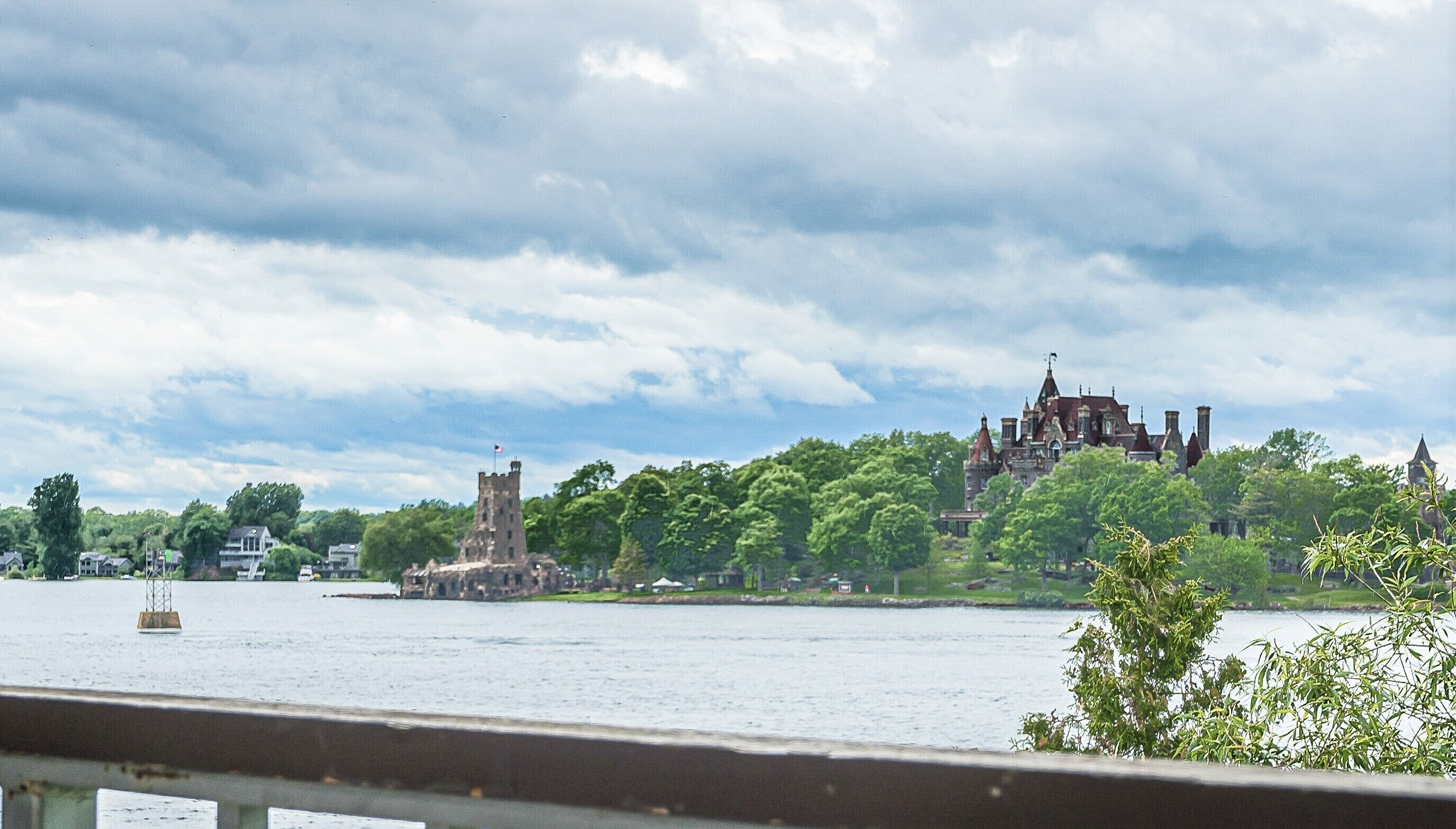A historic building with towers and a castle-like structure across a body of water, surrounded by lush greenery.
