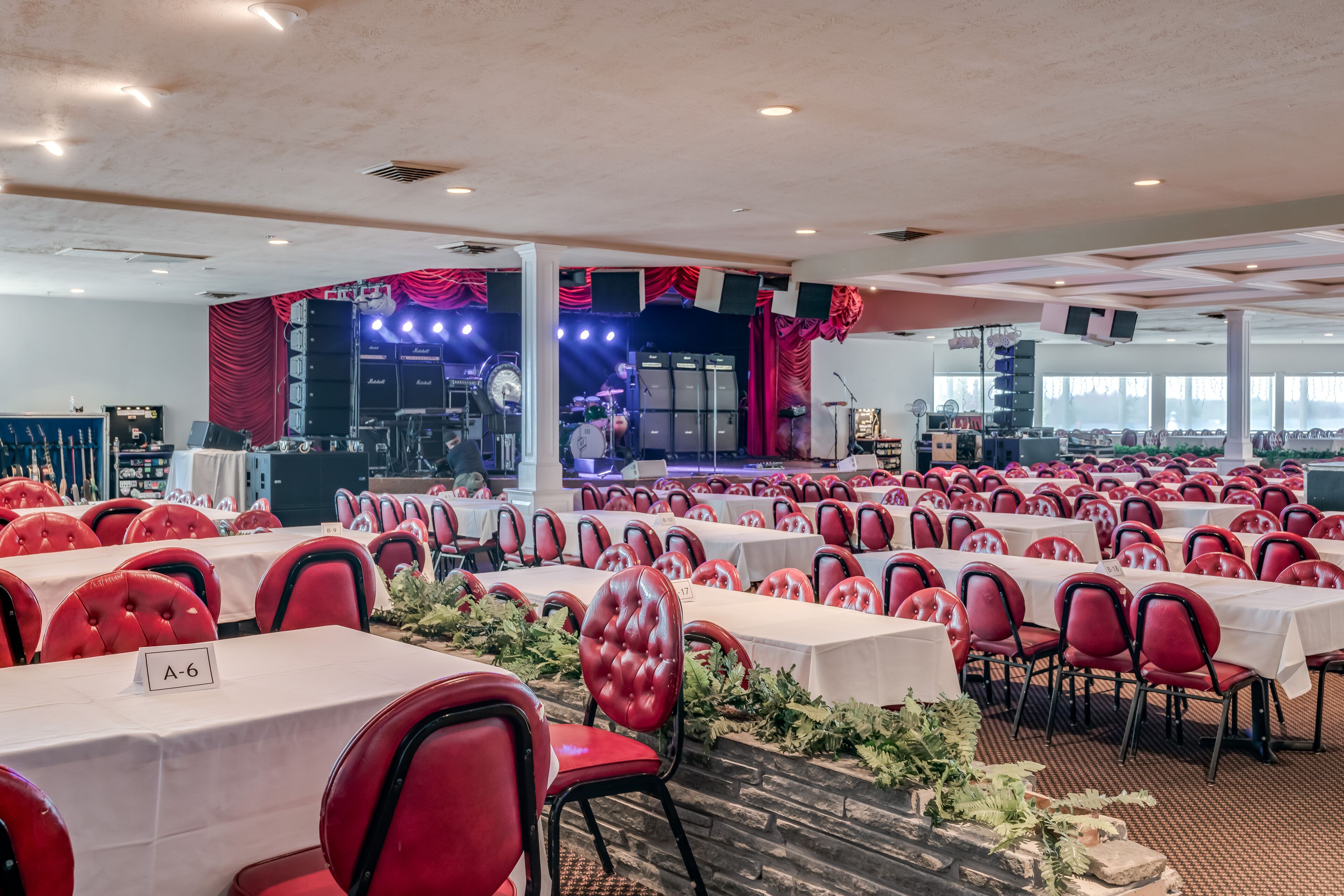 A banquet hall with rows of tables and chairs, a stage with musical equipment, and a view of the city.