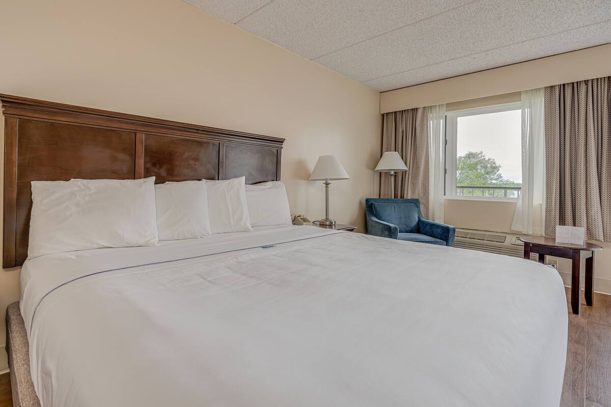 Een hotelkamer met een groot bed, een stoel, een lamp en een raam met gordijnen.