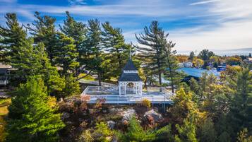 A gazebo with a pointed roof surrounded by dense trees and a clear sky.