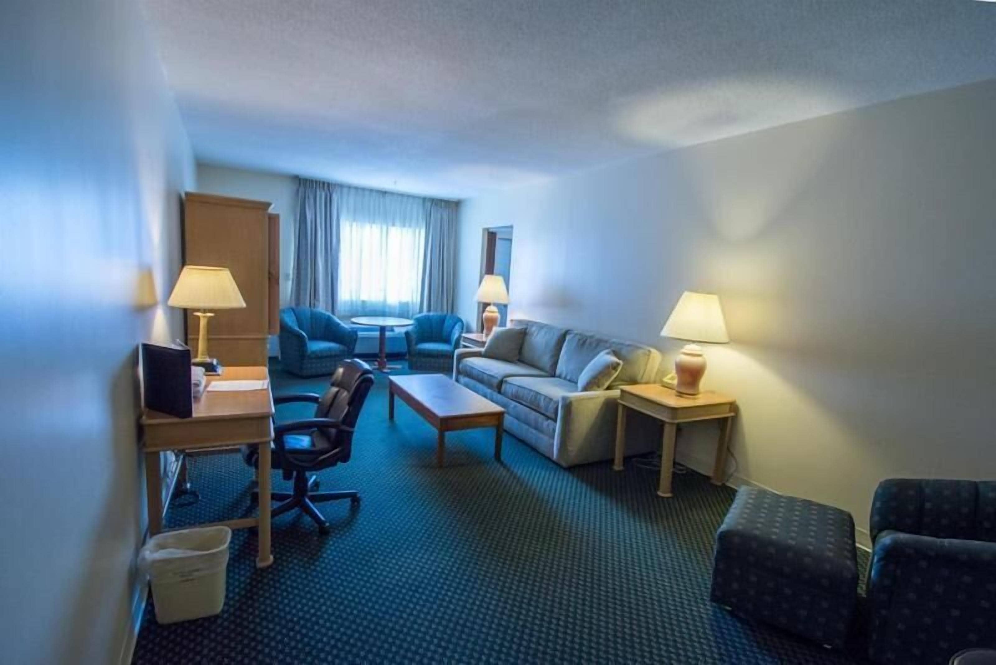 A hotel room with a desk, two armchairs, a sofa, and a small table.