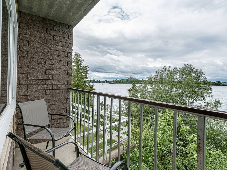 A balcony with a view of a lake, a brick wall, and a chair.