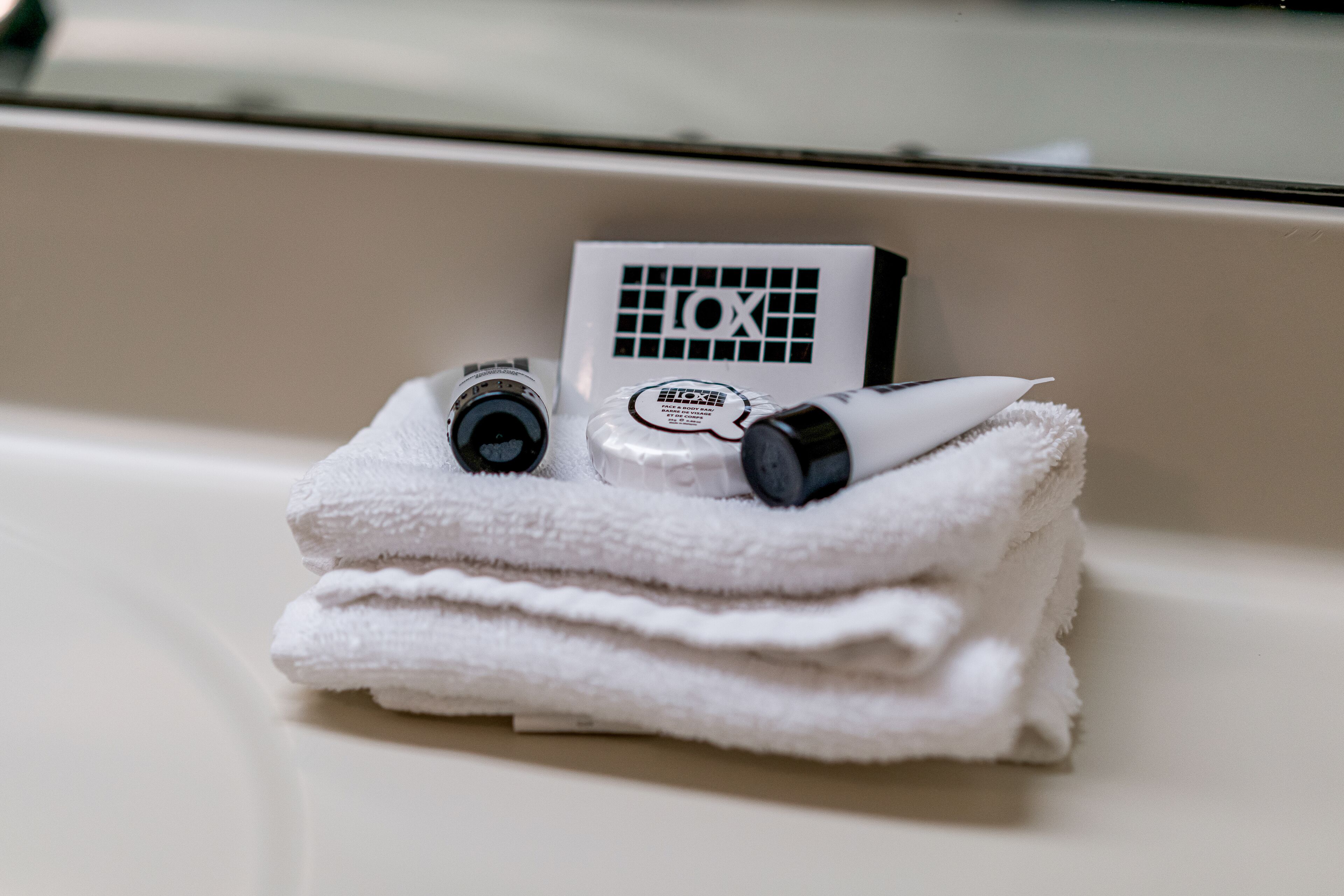A stack of white towels with a bottle of lotion and a bottle of shampoo on top.