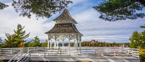 A white gazebo with a pointed roof, surrounded by a white fence and set on rocky terrain.