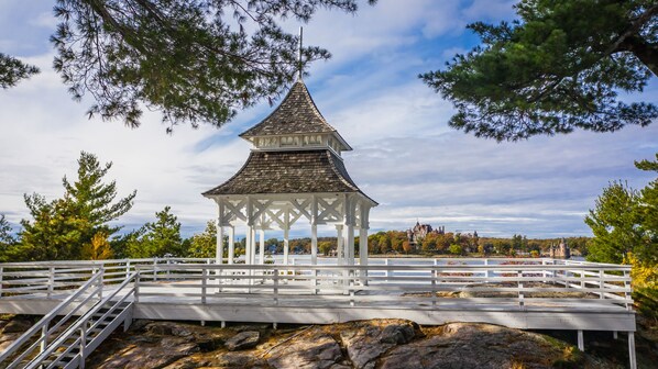 A white gazebo with a pointed roof, surrounded by a white fence and set on rocky terrain. - Bonnie Castle Resort & Marina (Alexandria Bay)