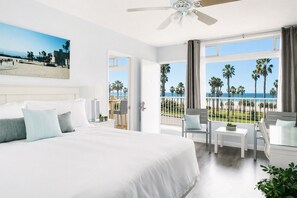 Habitación de hotel con una cama grande, un balcón con vistas a la playa y un ventilador de techo.