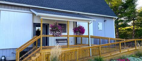 A building with a wooden deck and stairs leading to a porch with hanging flower baskets.