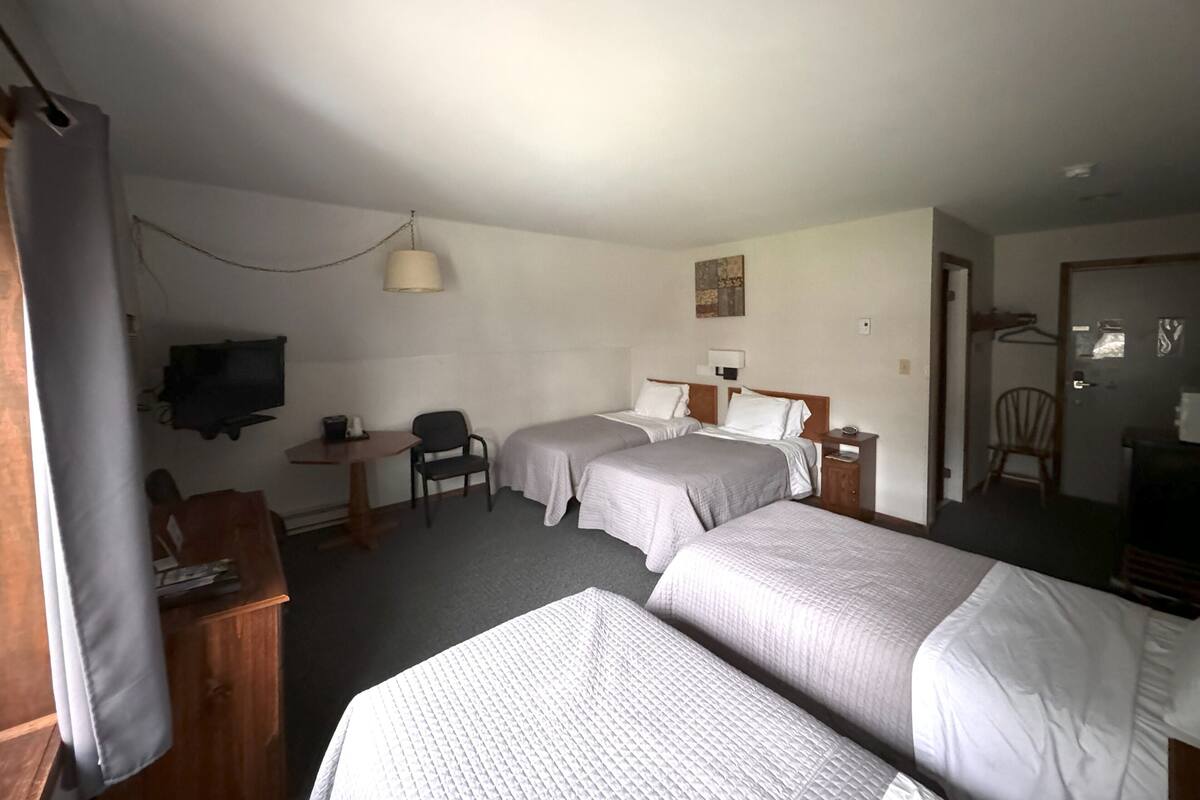 A hotel room with two beds, a desk, a chair, a television, and a small table.