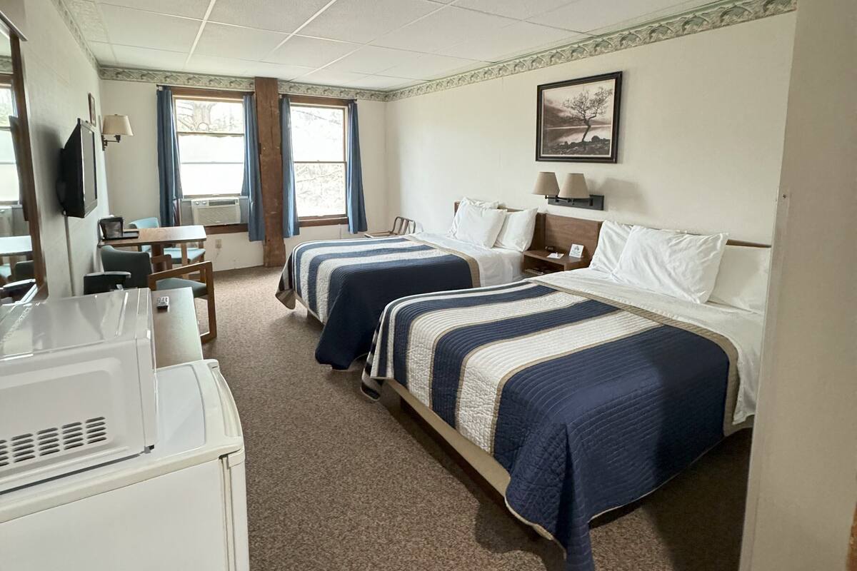 A hotel room with two beds, a desk, a television, and a window with curtains.