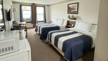 A hotel room with two beds, a desk, a television, and a window with curtains.