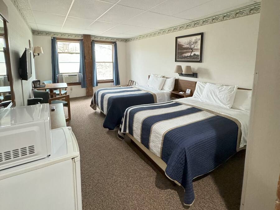 A hotel room with two beds, a desk, a television, and a window with curtains.