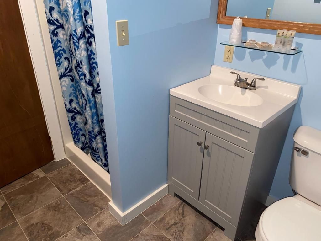 A bathroom with a white sink, grey cabinets, a blue wall, and a toilet.
