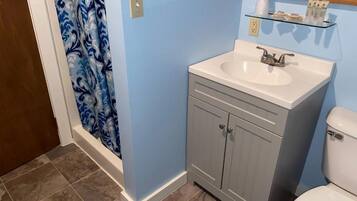 A bathroom with a white sink, grey cabinets, a blue wall, and a toilet.