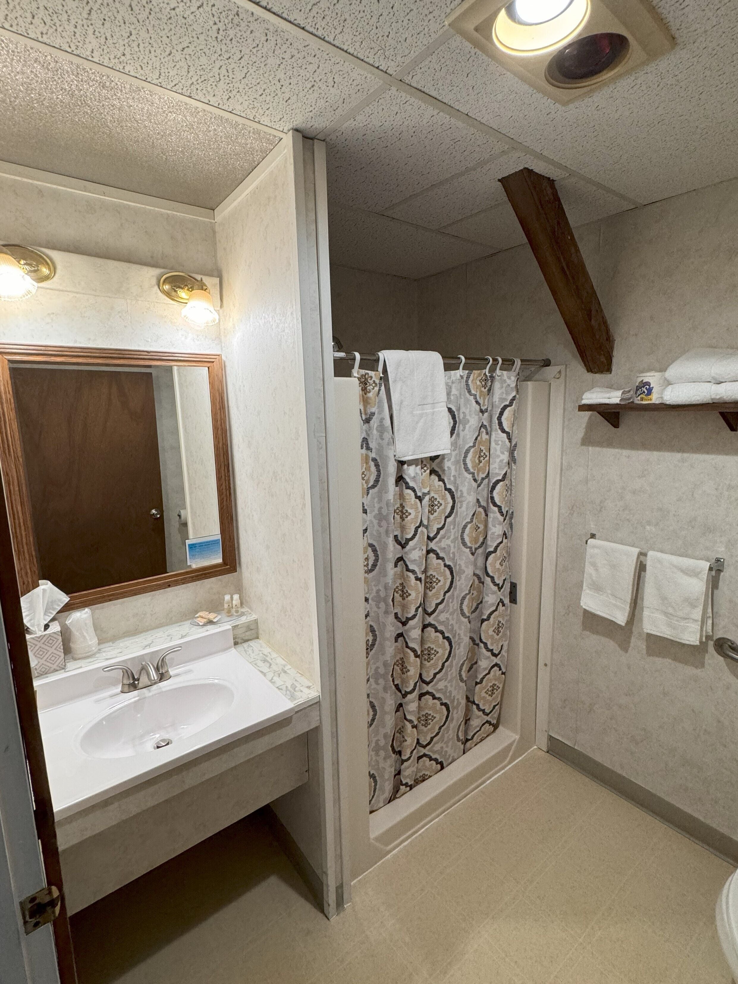 Un baño con lavamanos, espejo, cortina de ducha y toallero.