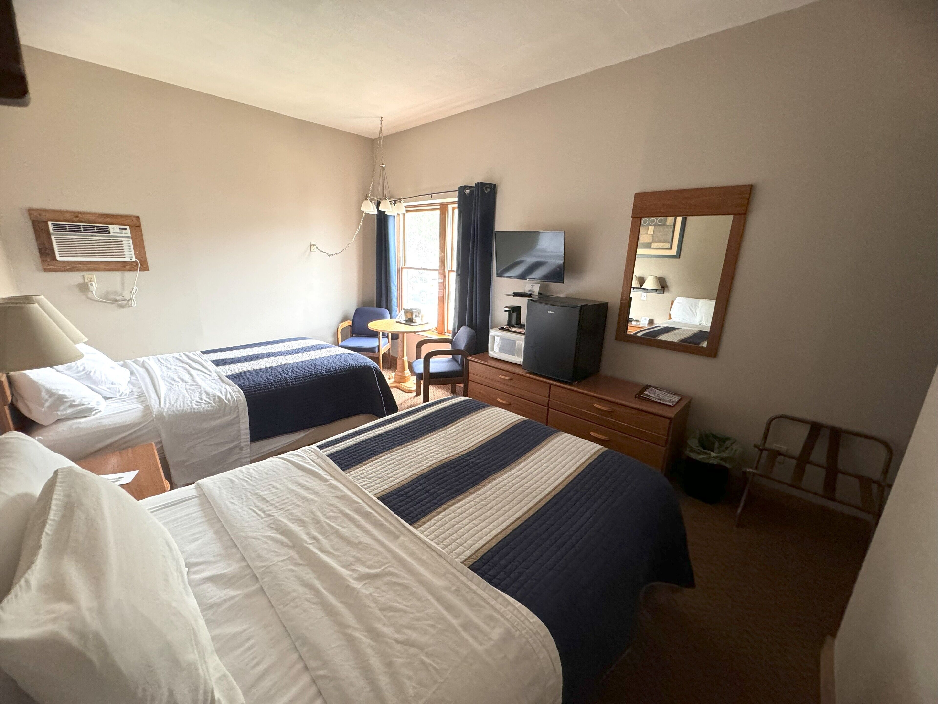 A hotel room with two beds, a desk, a television, a mirror, and a window with curtains.
