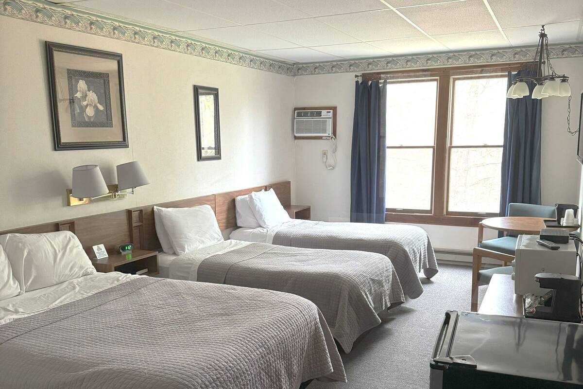 A hotel room with two beds, a desk with a chair, a telephone, and a window with curtains.