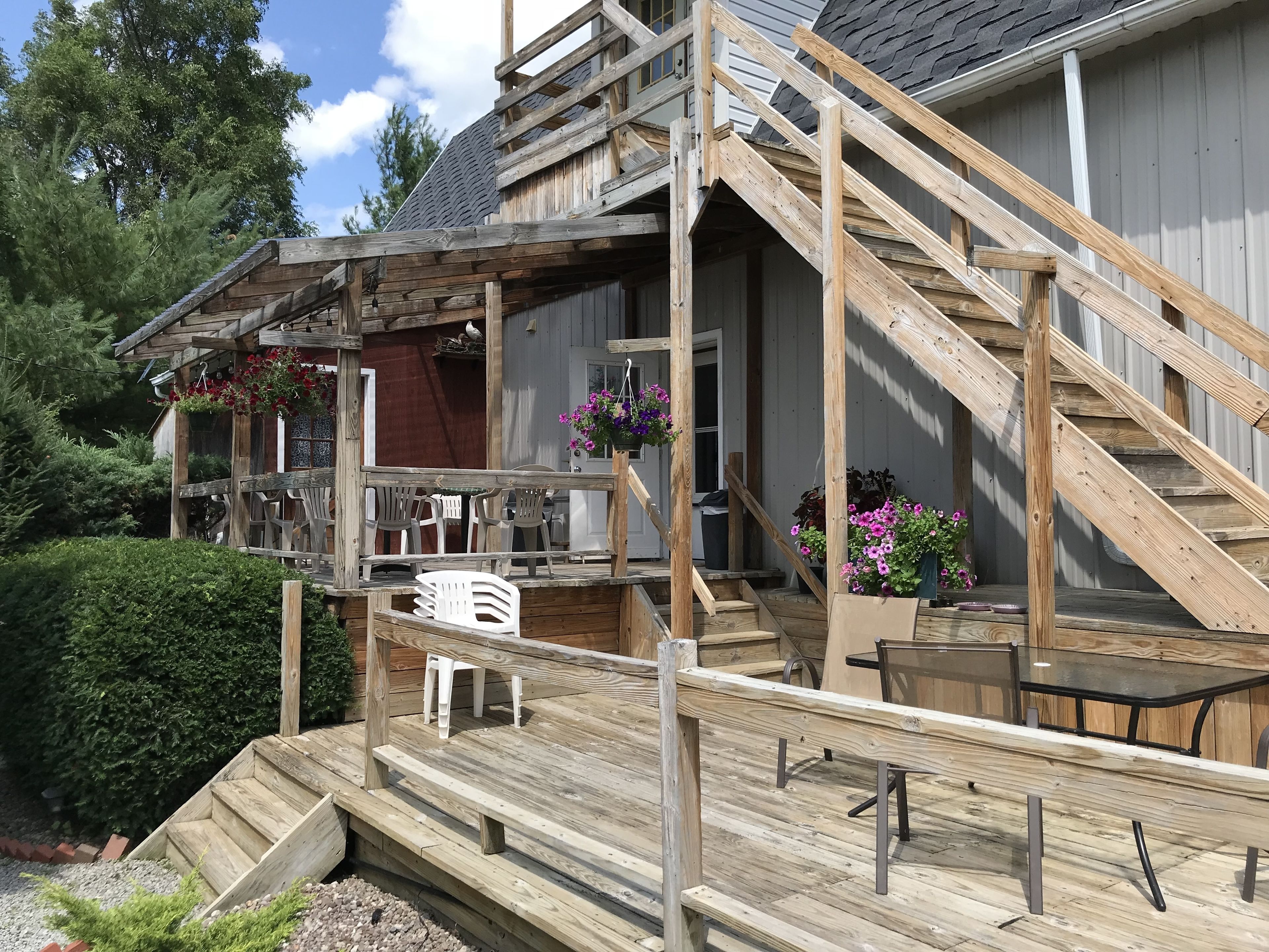 Een houten terras met buitenmeubilair en een trap die leidt naar een overdekt gedeelte met bloembakken.
