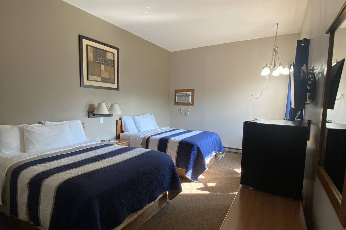 A hotel room with two beds, a desk, a chair, a TV, and a framed picture on the wall.