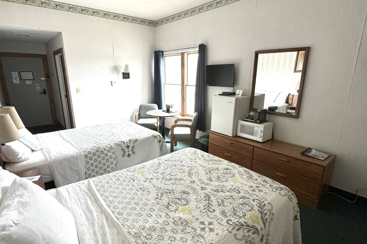 A hotel room with two beds, a desk with a chair, a microwave, a television, and a dresser.
