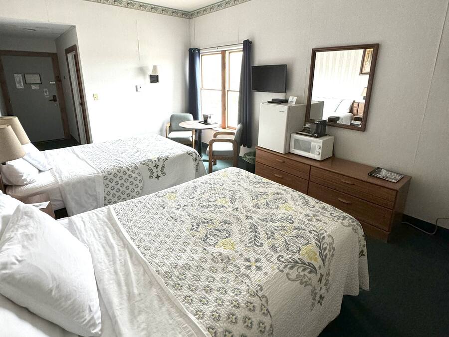 Camera d'albergo con due letti, una scrivania con sedia, forno a microonde, televisore e cassettiera.
