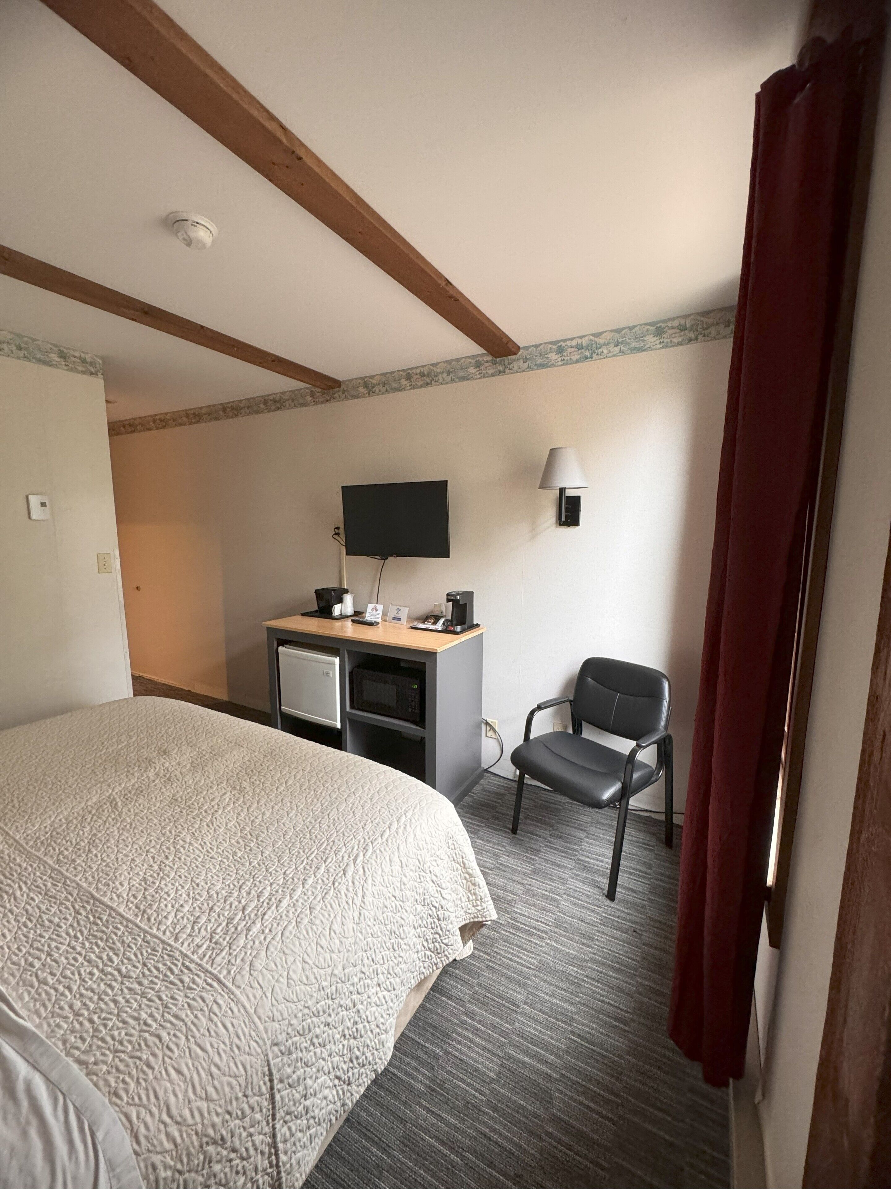 Una camera d'albergo con un letto, una scrivania con un computer, una sedia, una televisione e una lampada.