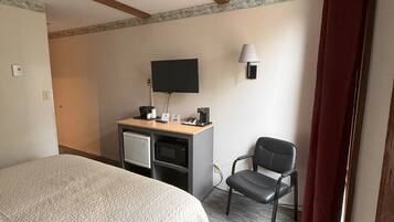 Una camera d'albergo con un letto, una scrivania con un computer, una sedia, una televisione e una lampada.