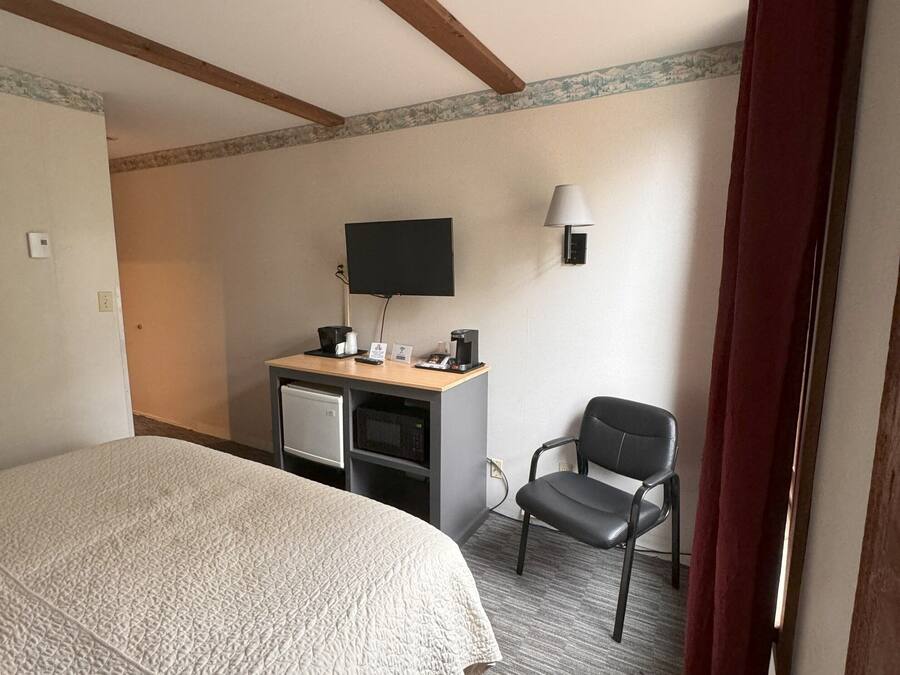 Una camera d'albergo con un letto, una scrivania con un computer, una sedia, una televisione e una lampada.