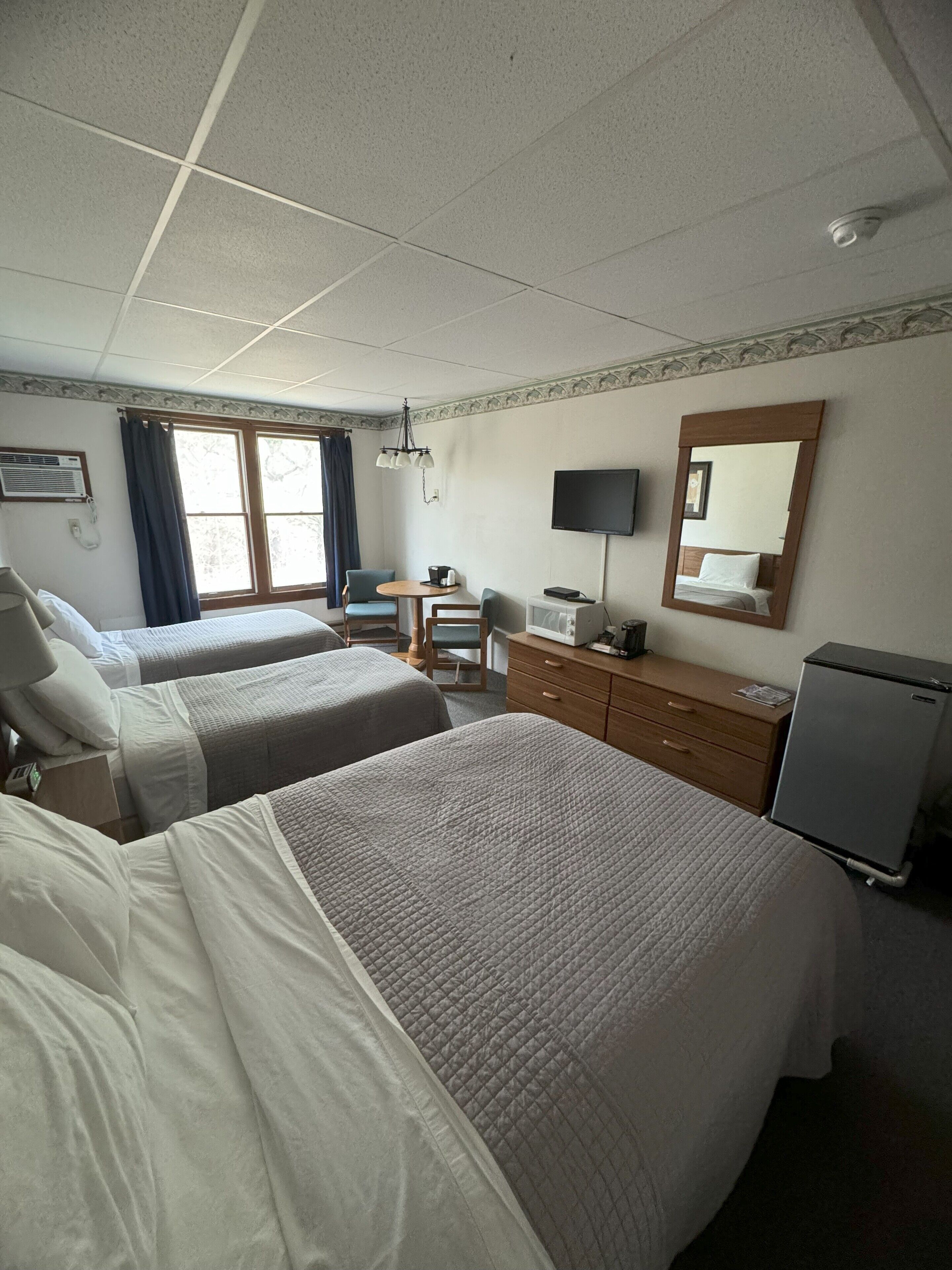 Quarto de hotel com duas camas, uma escrivaninha, televisão, espelho e frigorífico.