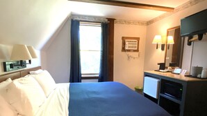 Ein Hotelzimmer mit einem Bett, einem Schreibtisch mit Computer, einem Spiegel und einem Fenster mit Vorhängen.