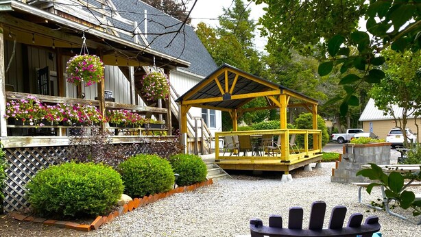 Ein Holzhaus mit überdachter Terrasse, Kiesweg und blauem Adirondack-Sessel.