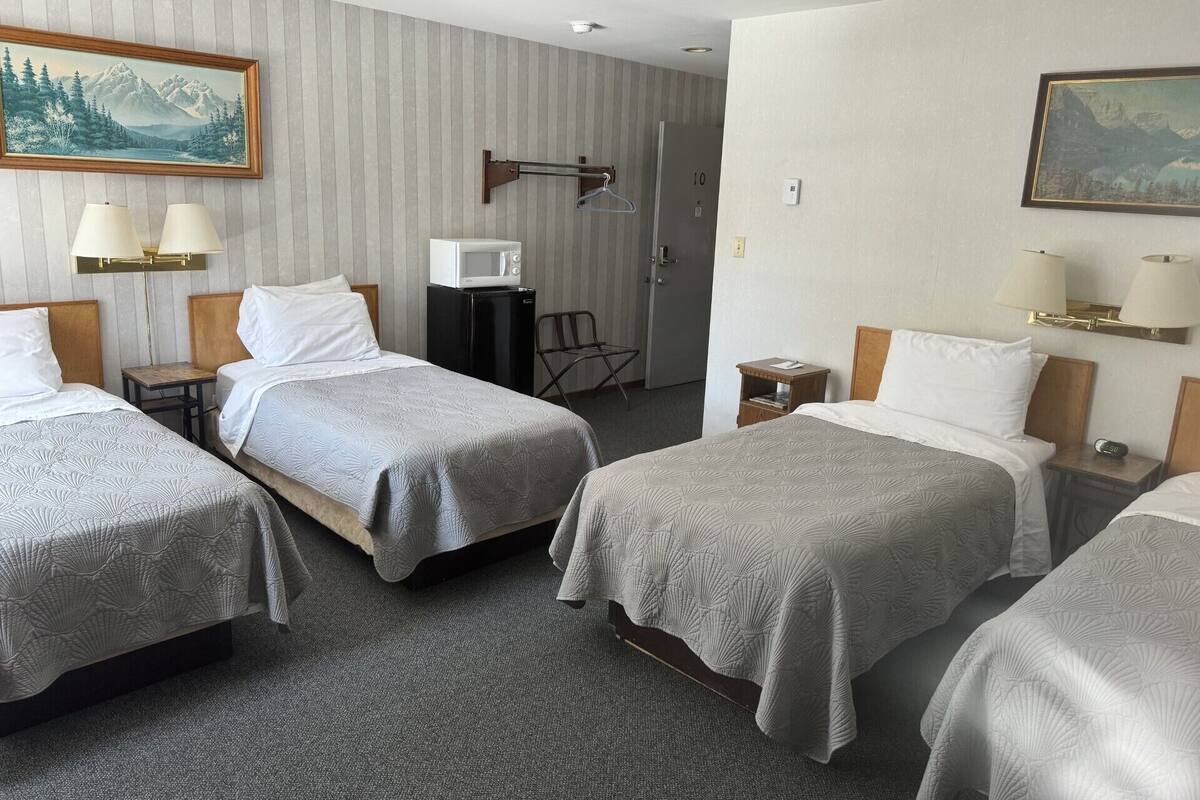 A hotel room with three beds, a microwave, a small table, and a chair.