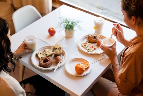 Une table à manger avec des assiettes remplies de nourriture, une tasse de café et une plante.