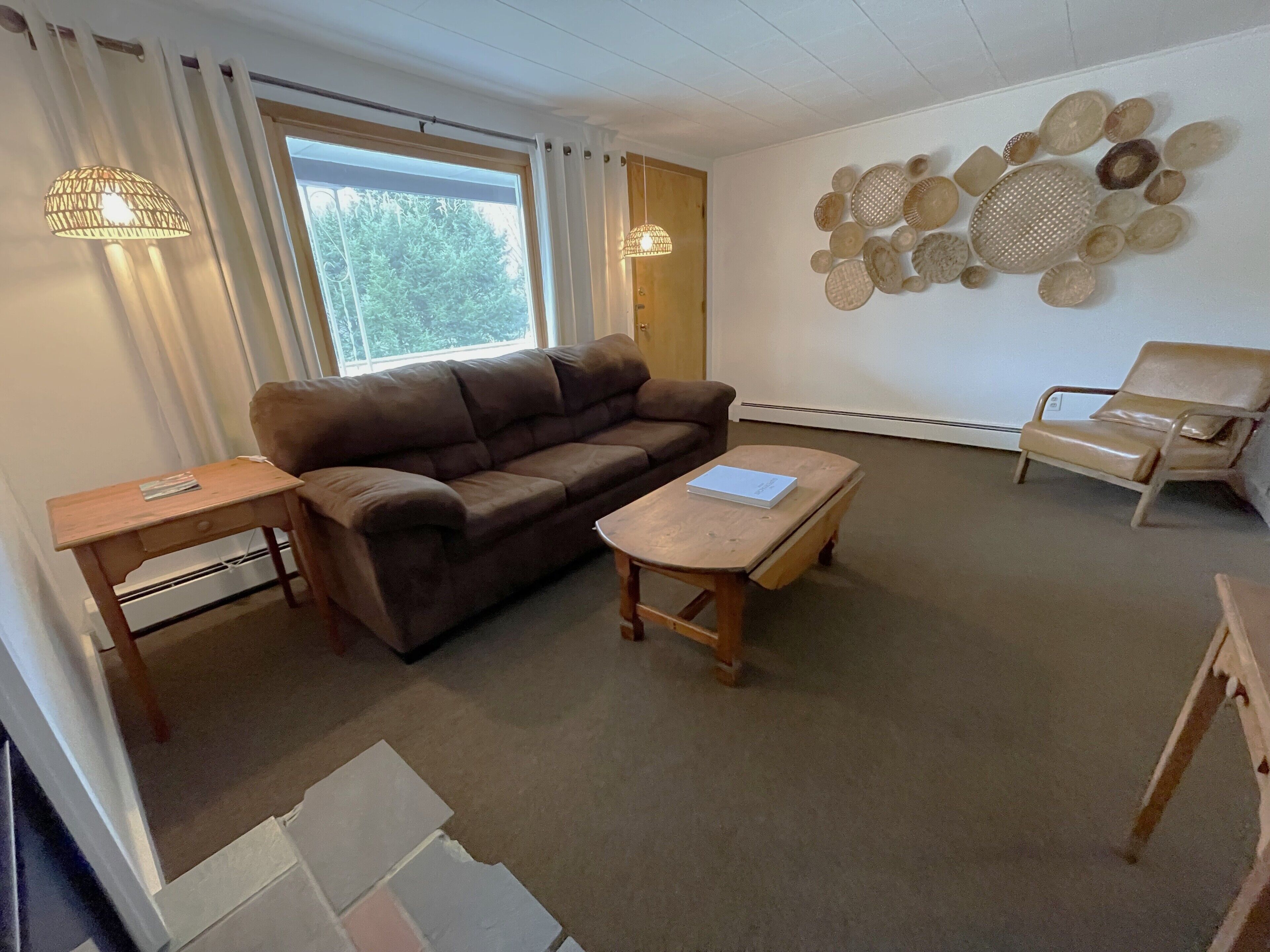 A living room with a brown sofa, a wooden coffee table, a side table, a beige armchair, and a wall with decorative plates.