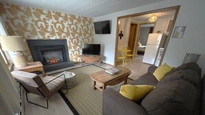 Una sala de estar con chimenea, sofá, sillón y televisor.