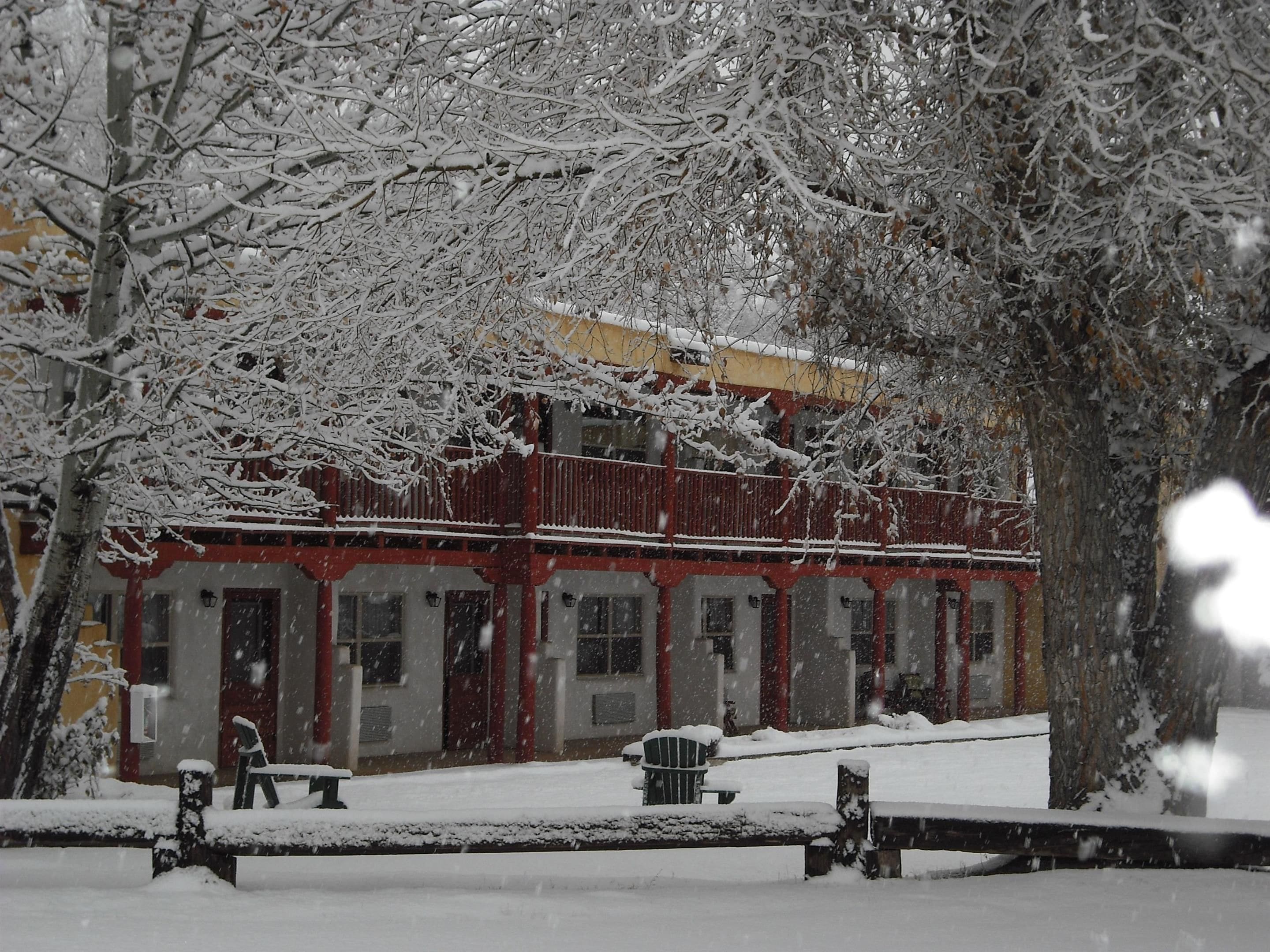 Un edificio con fachada roja y detalles blancos, rodeado de árboles cubiertos de nieve.