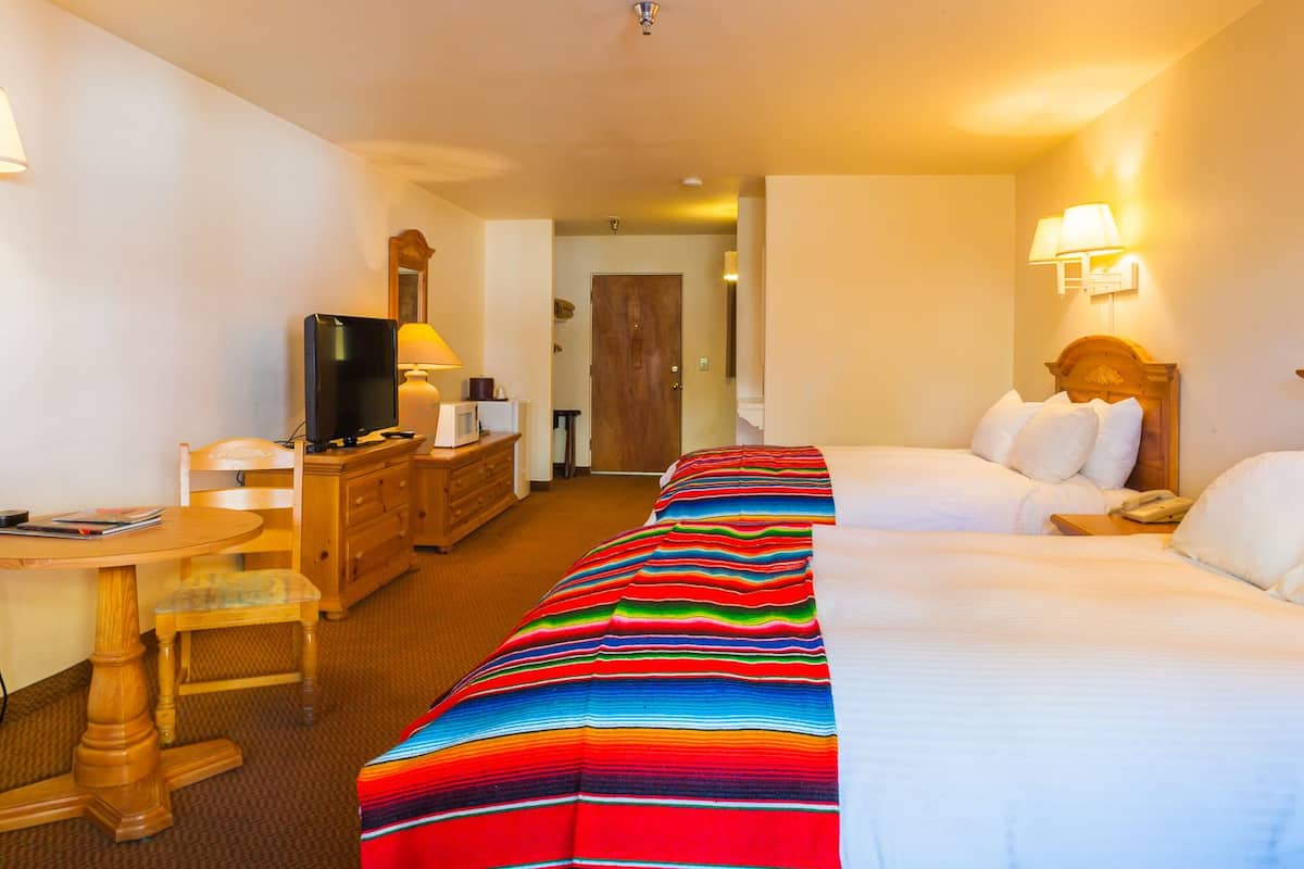 A hotel room with a bed, a desk with a television, a dresser, and a colorful striped blanket.