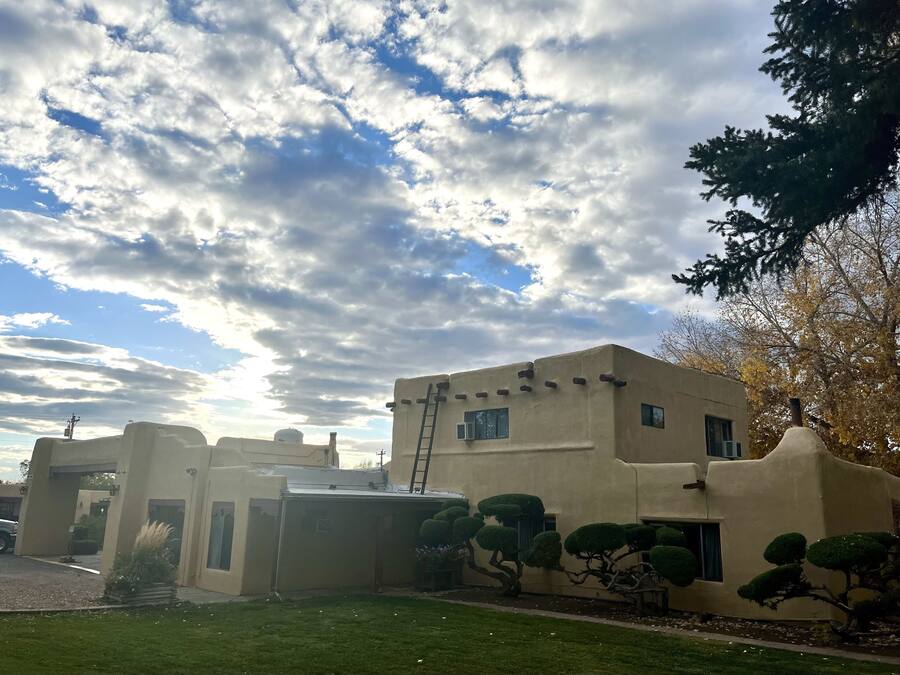 Un edificio con techo plano y una pequeña estructura adosada, rodeado de césped cuidado y árboles.