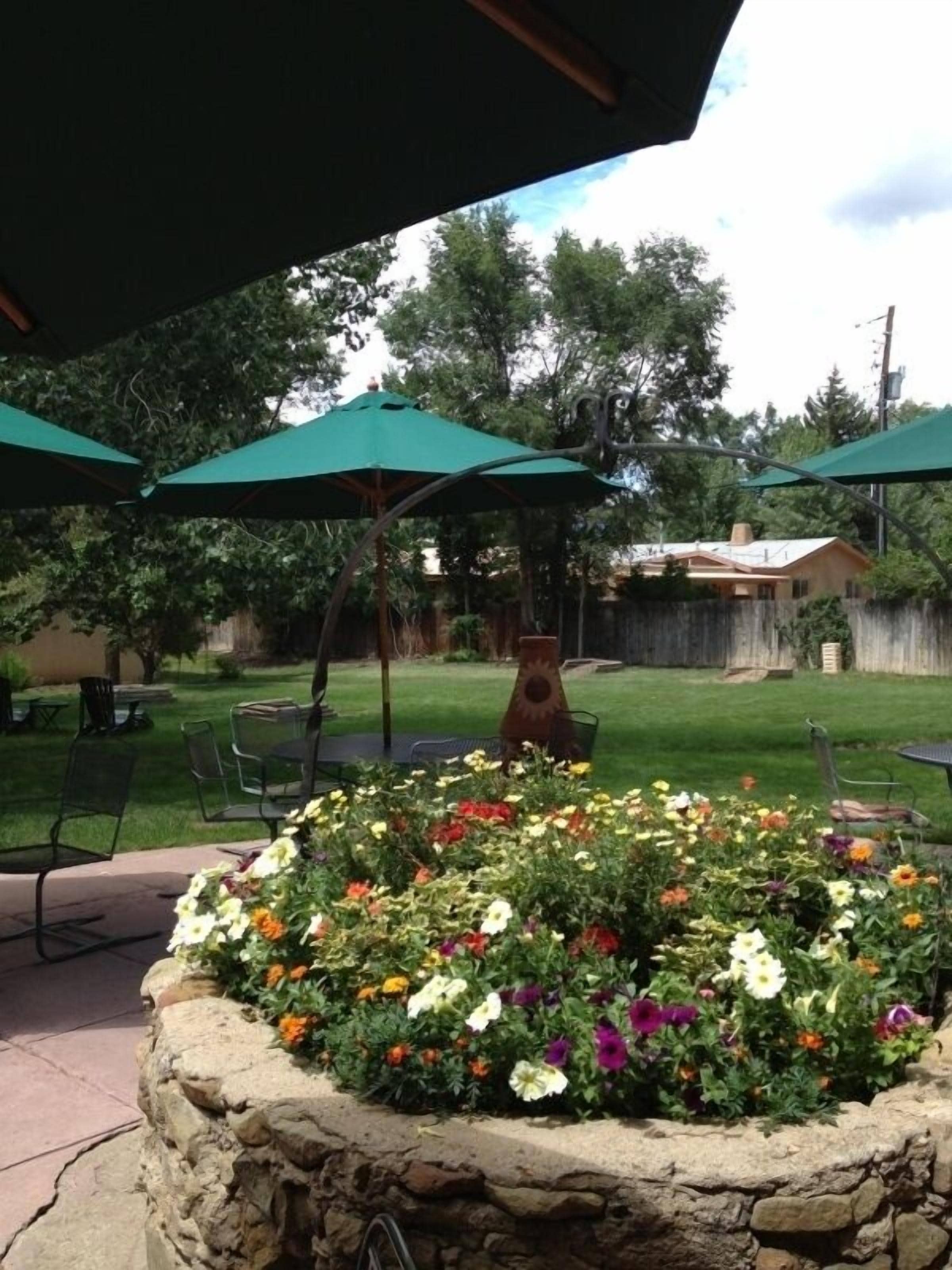A patio area with stone planters of colorful flowers, green umbrellas, and outdoor furniture.