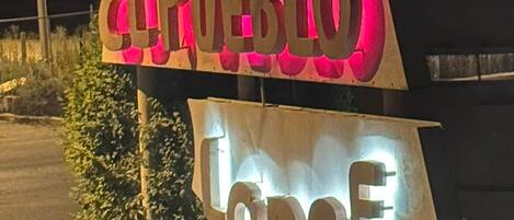 A sign for 'El Pueblo Lodge' with illuminated letters and a blue light on top.