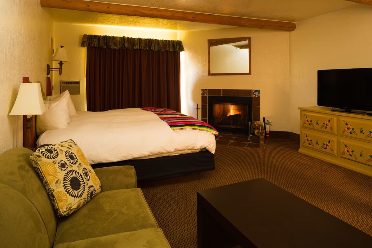 A hotel room with a bed, a sofa, a TV, a fireplace, and a mirror.