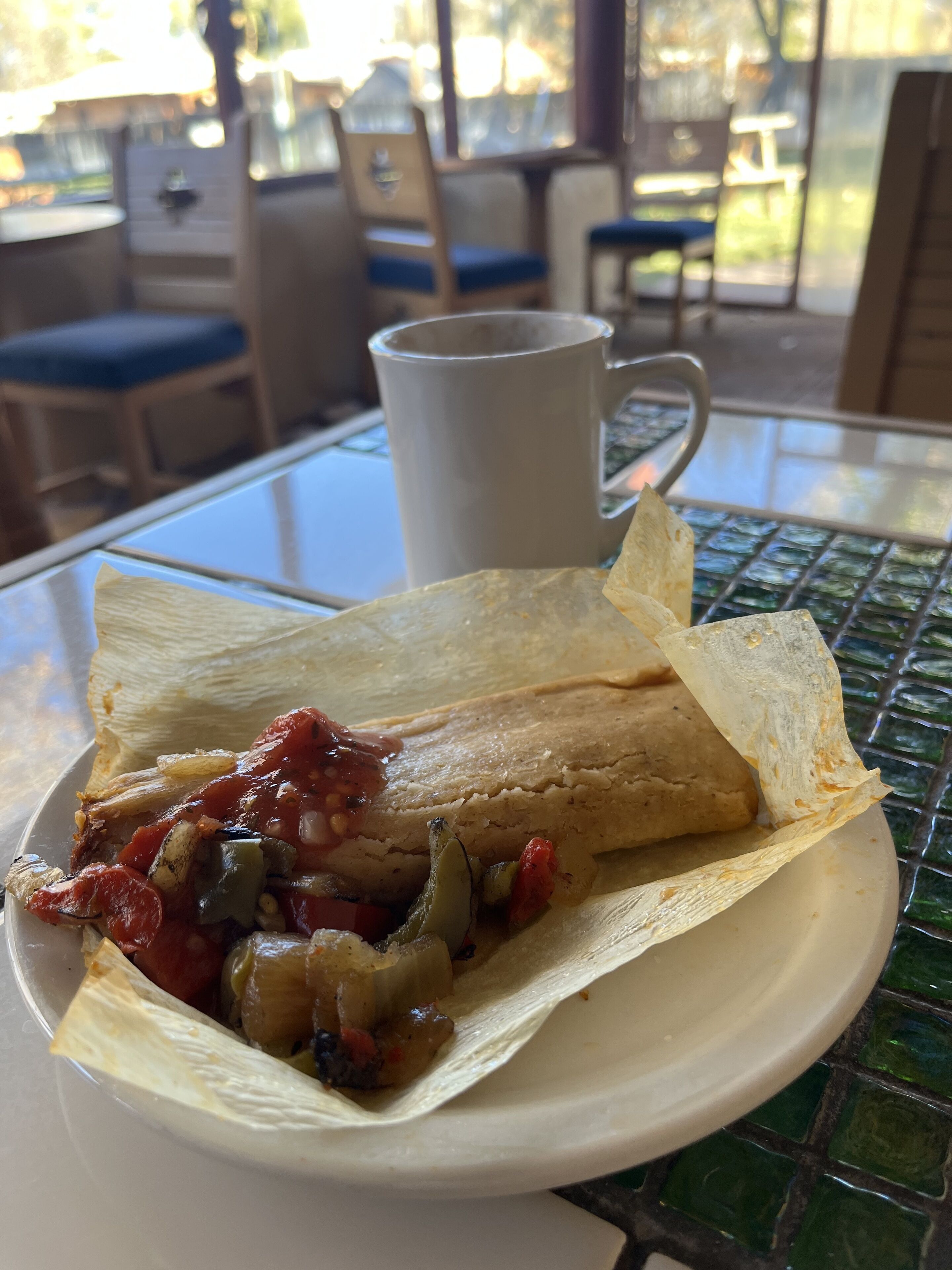 A plate with a crepe topped with vegetables and sauce, a white mug, and a glass table.