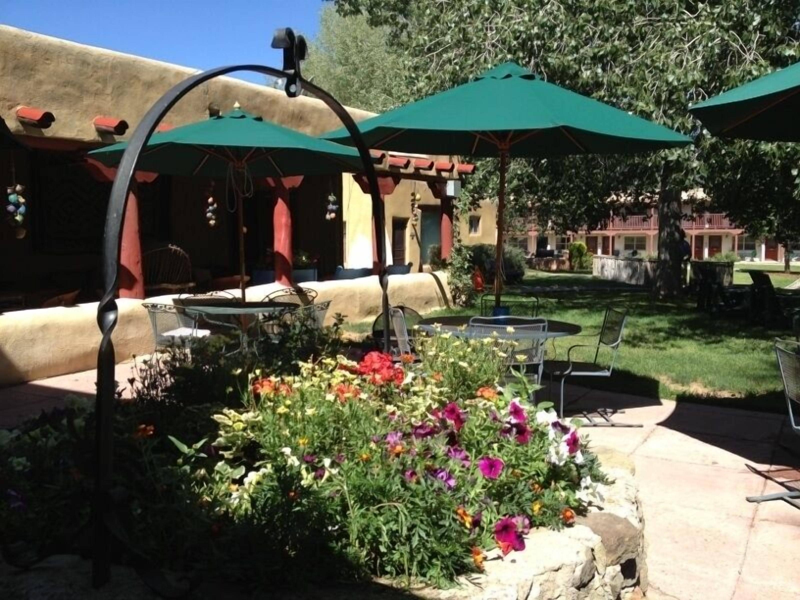 An outdoor patio area with green umbrellas, a stone planter with colorful flowers, and outdoor seating.