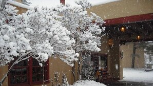 A snow-covered building with a red window frame and a snow-covered bush in front. - El Pueblo Lodge (Taos)