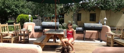 A patio with outdoor furniture, a dog, and a woman sitting under a green umbrella.