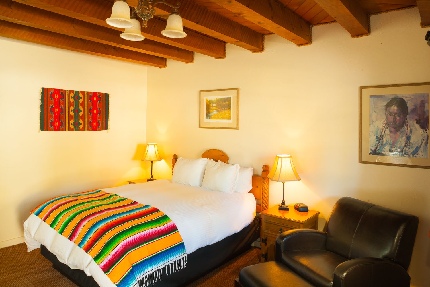 Habitación de hotel con cama, dos lámparas de noche, una silla y obras de arte en las paredes.